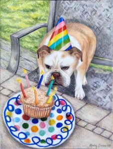 little bull dog standing in a chair. He wears a striped party hat and is looking at a birthday cake with candles on a polka dot paper plate