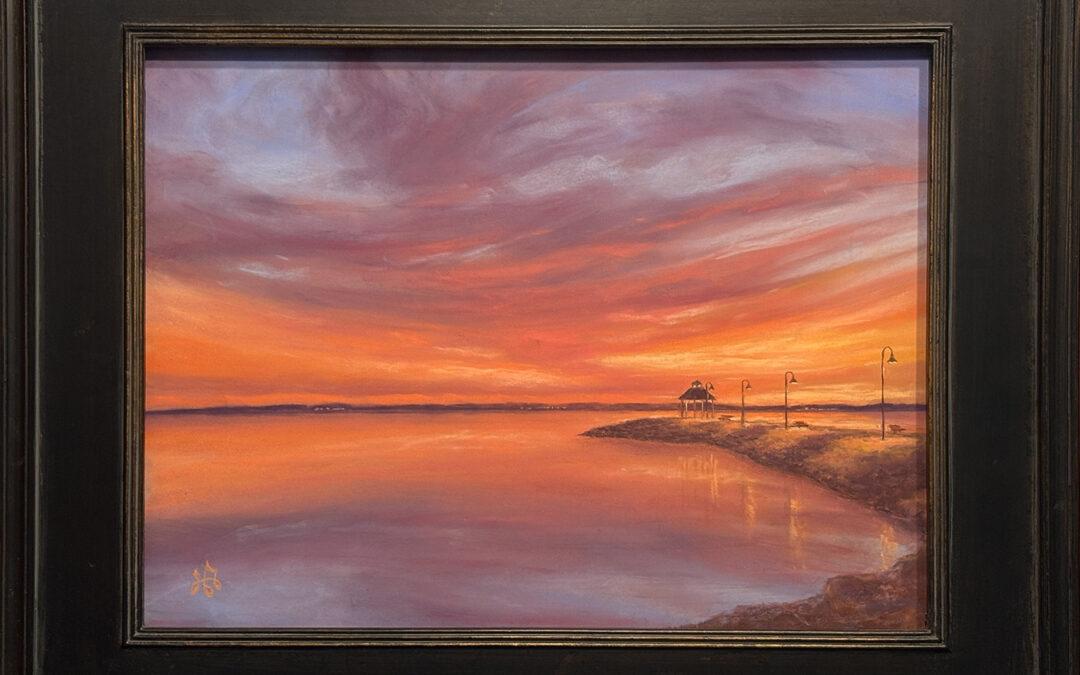 painting of a colorful orange and purple sunset. The reflection of the sky in water is separated by a distant horizon. On the right, a building and poles on a jut of land, lead the viewer back to the center and the sunset
