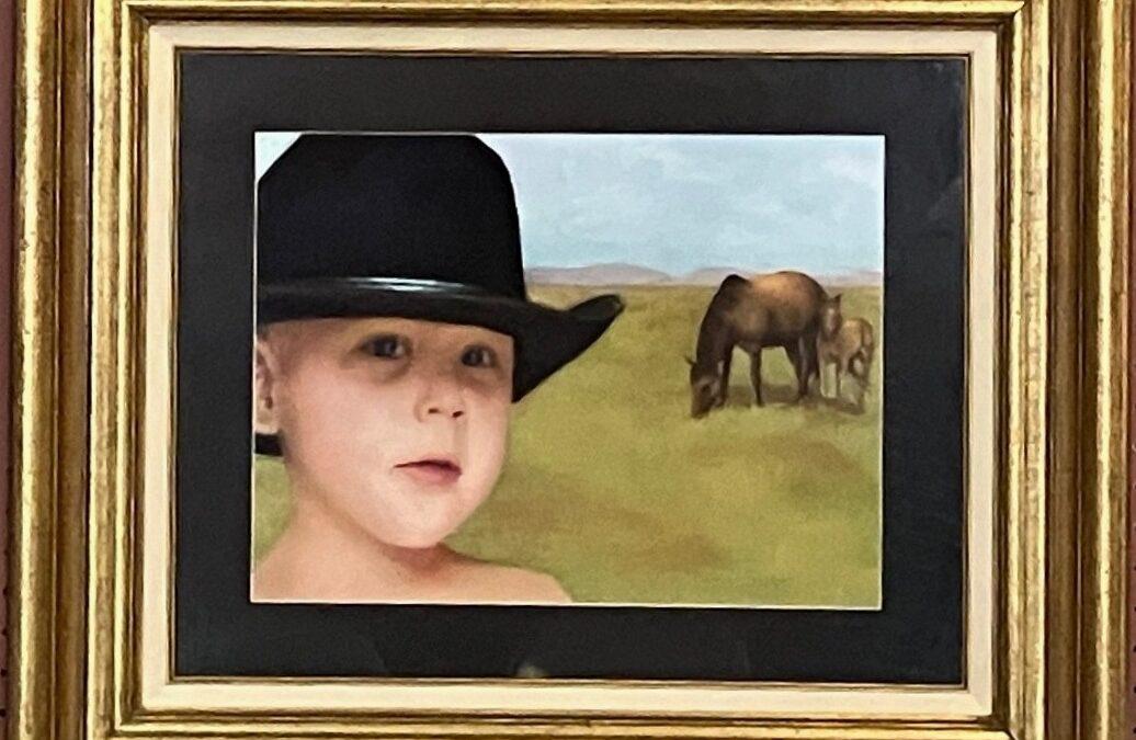 pastel painting of a young child wearing a black cowboy hat. We see the child up close in the foreground with a horse and colt in the background grazing on the prairie